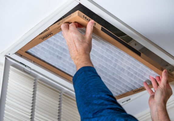 Man replacing dirty HVAC air filter in ceiling vent. Home air duct system maintenance for clean air.